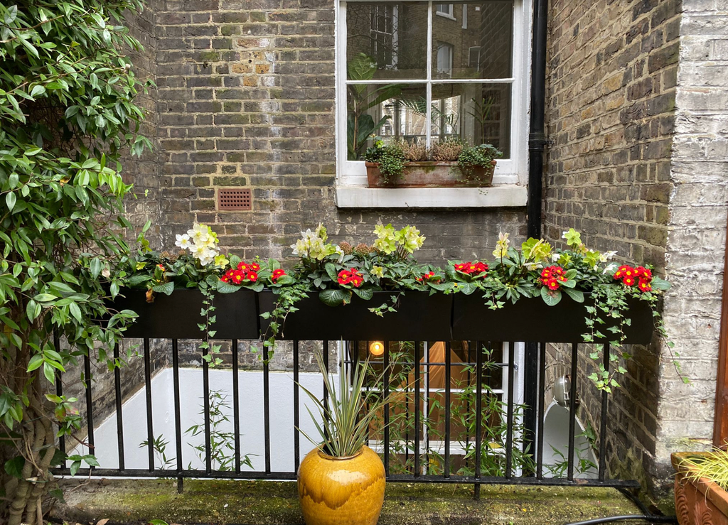 Decorative flower box with red and white flowers on a black metal railing against a brick wall.